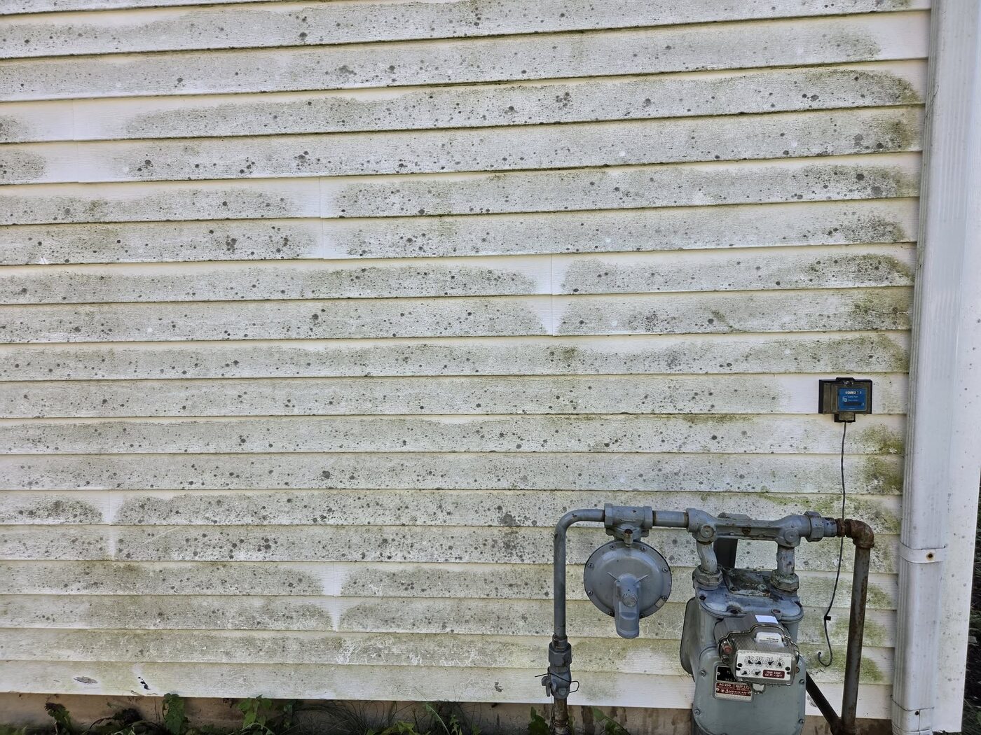 A wall of white siding dulled and streaked with dirt around the gas meter