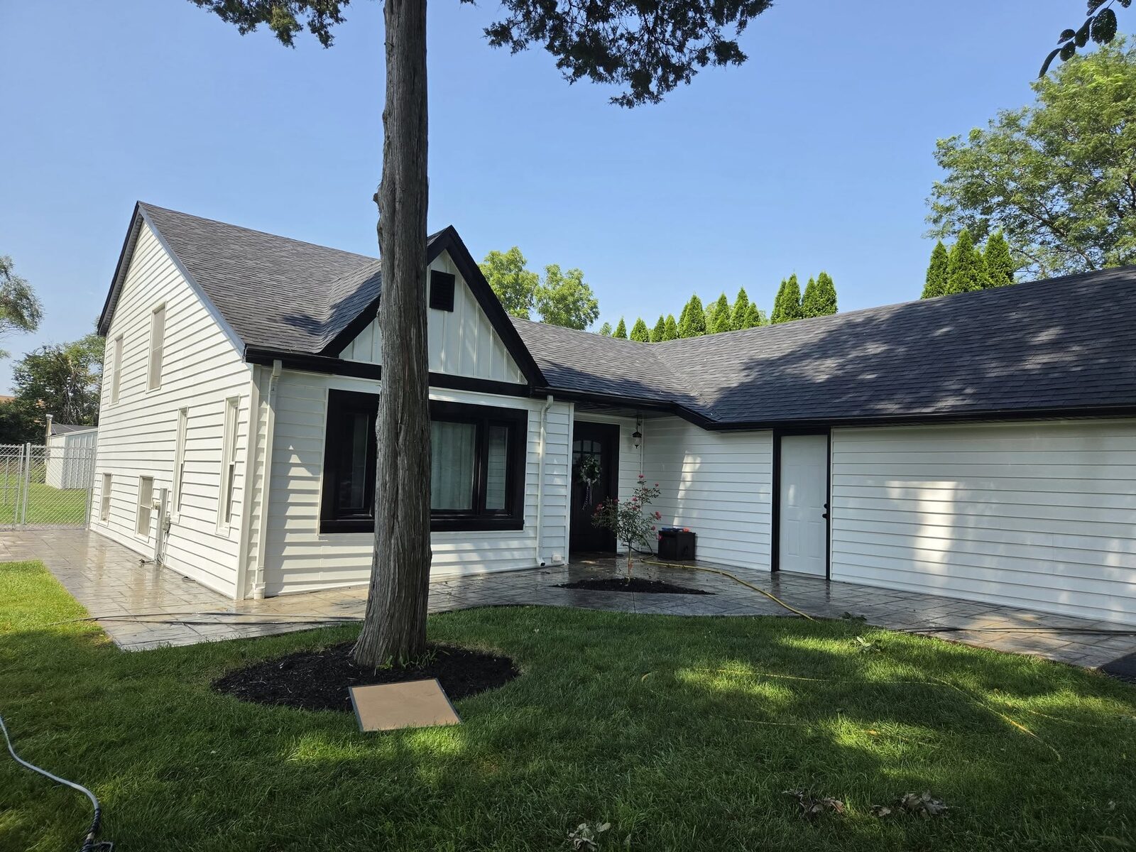 A white house and attached garage after washing, the siding and trim clean with fresh mulch beds at the front